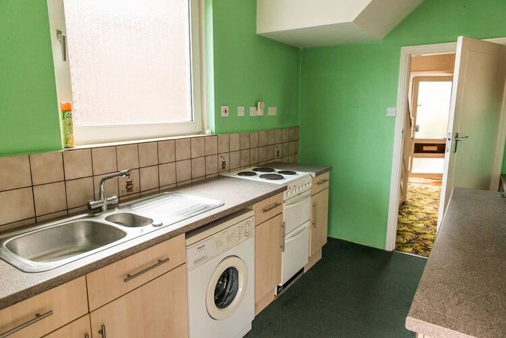 an empty kitchen with green walls and white appliances on the counter top, next to a washer and dryer