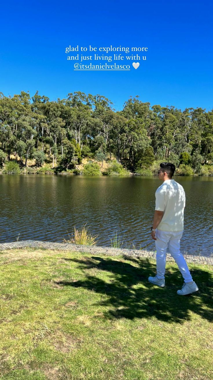 a man standing on top of a lush green field next to a lake