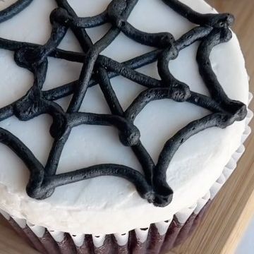 a cupcake decorated with black icing and spider webs on the top is sitting on a wooden table