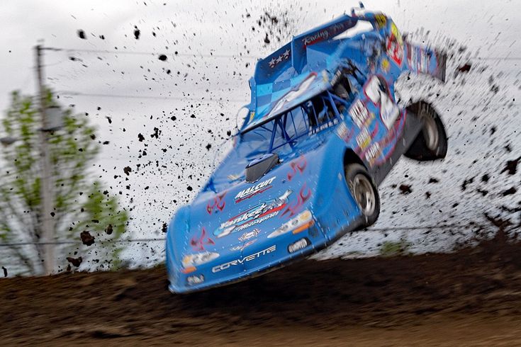 a blue car is in the air after it was hit by a truck on a dirt track