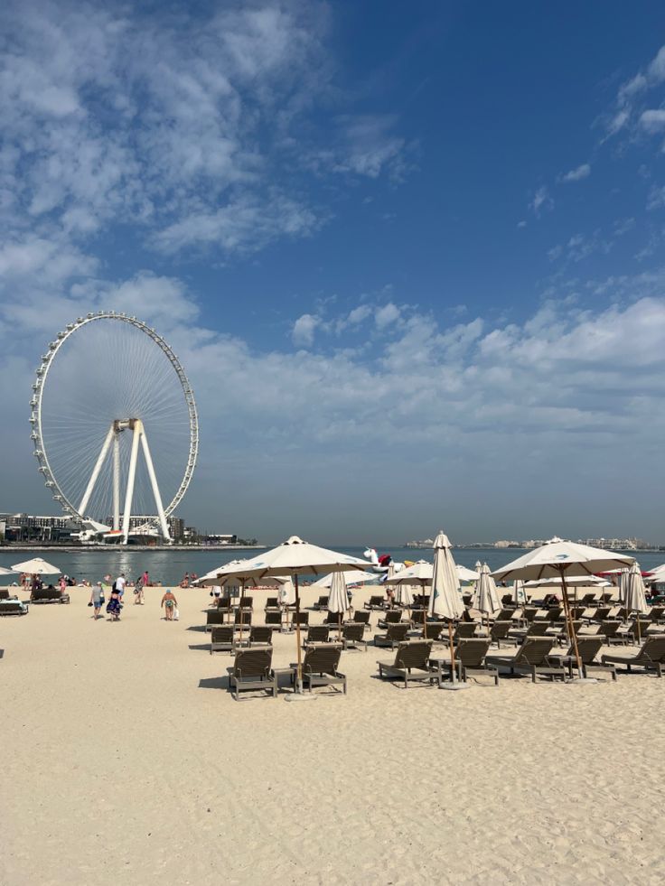 chairs and umbrellas are set up on the beach with a ferris wheel in the background