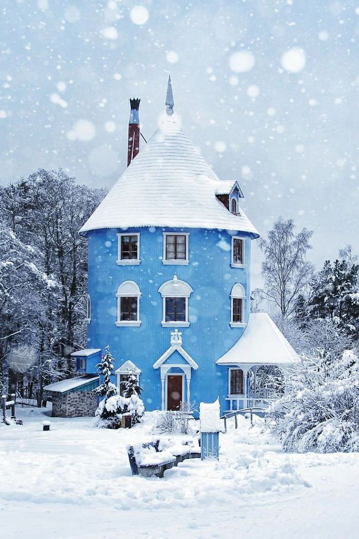 a blue house is covered in snow and surrounded by trees