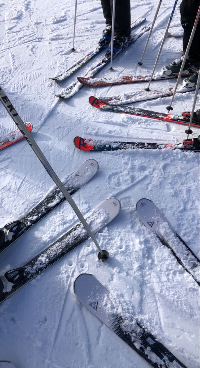 several pairs of skis and poles in the snow with people standing around on it