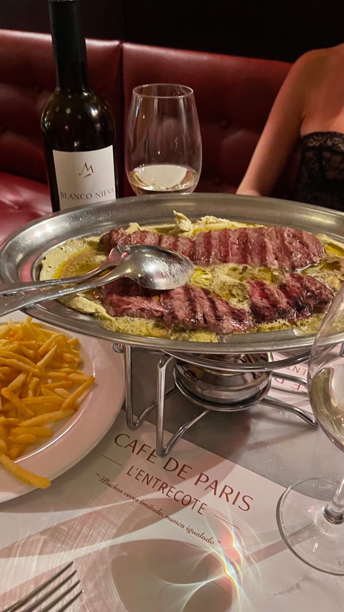 a woman sitting at a table in front of a platter of food and wine