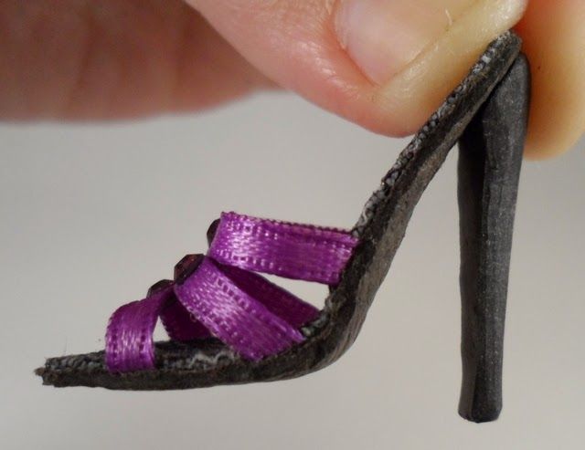 a hand holding a miniature shoe with purple ribbon