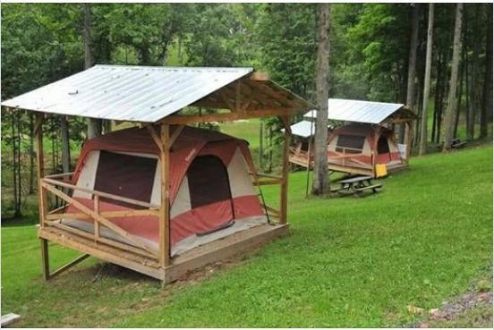 two tents are set up in the woods with picnic tables and benches around them for people to sit on