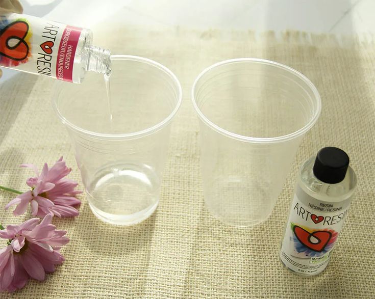 two plastic cups with one empty and the other half full, sitting on a table next to pink flowers