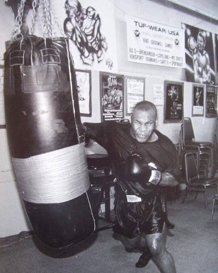 an old photo of a man wearing boxing gloves and holding a punching bag in a gym