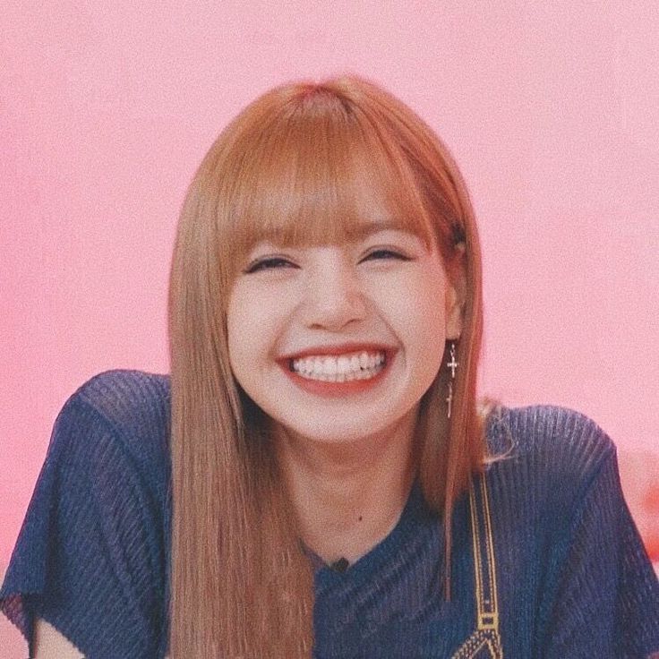 a woman with long hair smiling and wearing a blue shirt in front of a pink wall