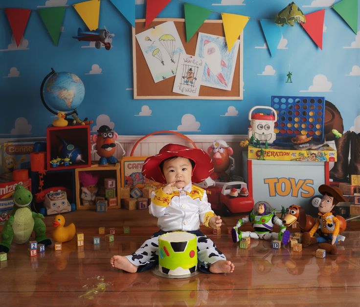 a baby sitting on the floor with toys in front of him and wearing a cowboy hat