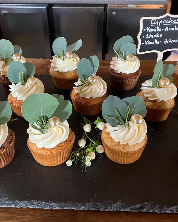 cupcakes with white frosting and greenery on top are sitting on a table