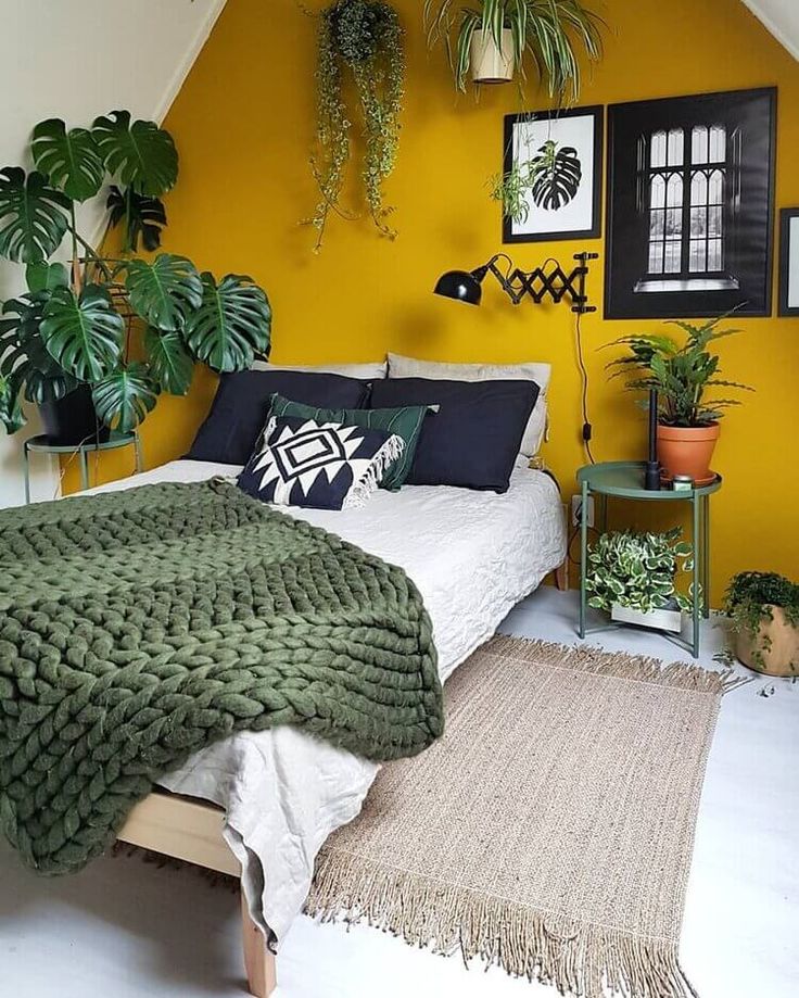 a bedroom with yellow walls and green plants on the wall above the bed, along with a rug