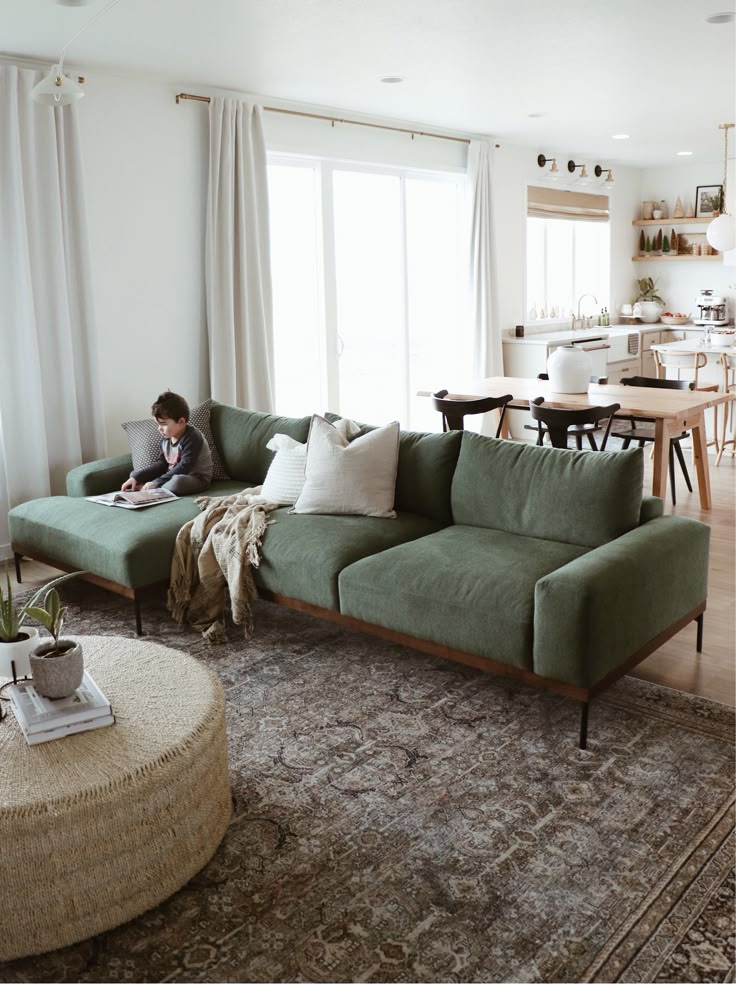 a woman sitting on top of a green couch in a living room next to a window