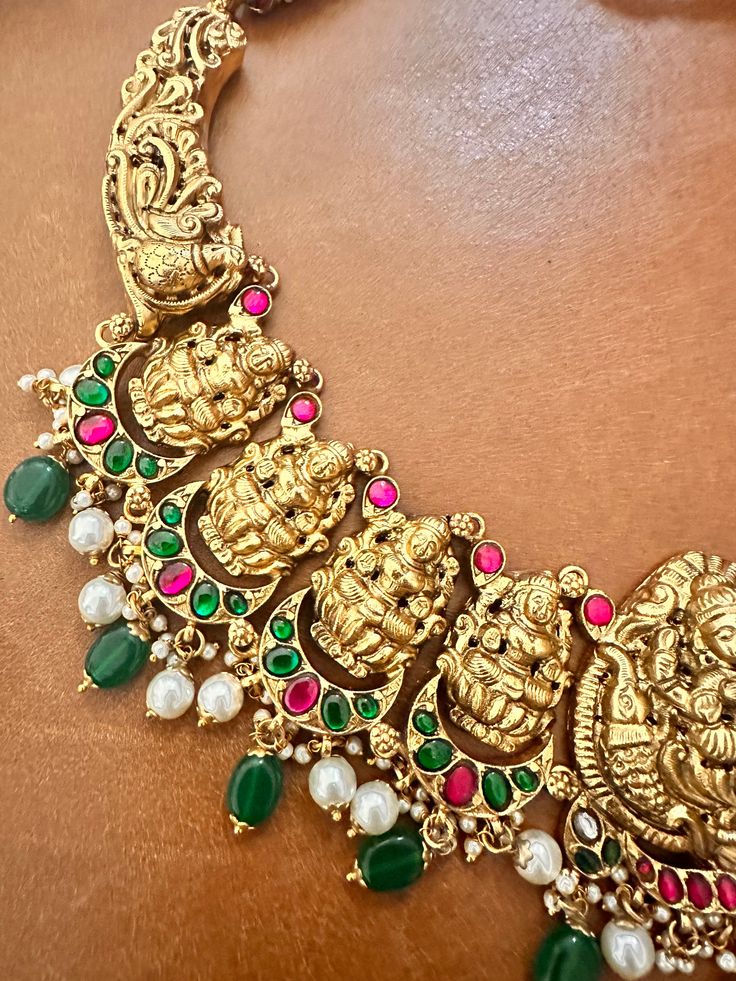 The Antique Kundan Lakshmi Necklace is a masterpiece of traditional Indian craftsmanship, representing the regal heritage of temple jewelry. At its centerpiece, it features a finely detailed depiction of Goddess Lakshmi, the Hindu goddess of wealth and prosperity, intricately carved in gold. Surrounding the central deity are vibrant, hand-set Kundan gemstones—emeralds, rubies, and diamonds—arranged in floral and geometric patterns. The necklace is designed with each element embossed with antique Temple Necklace, Goddess Of Wealth, Hindu Goddess, Temple Jewelry, Wealth And Prosperity, Goddess Dress, The Hindu, Necklace Bridal, Kundan Earrings