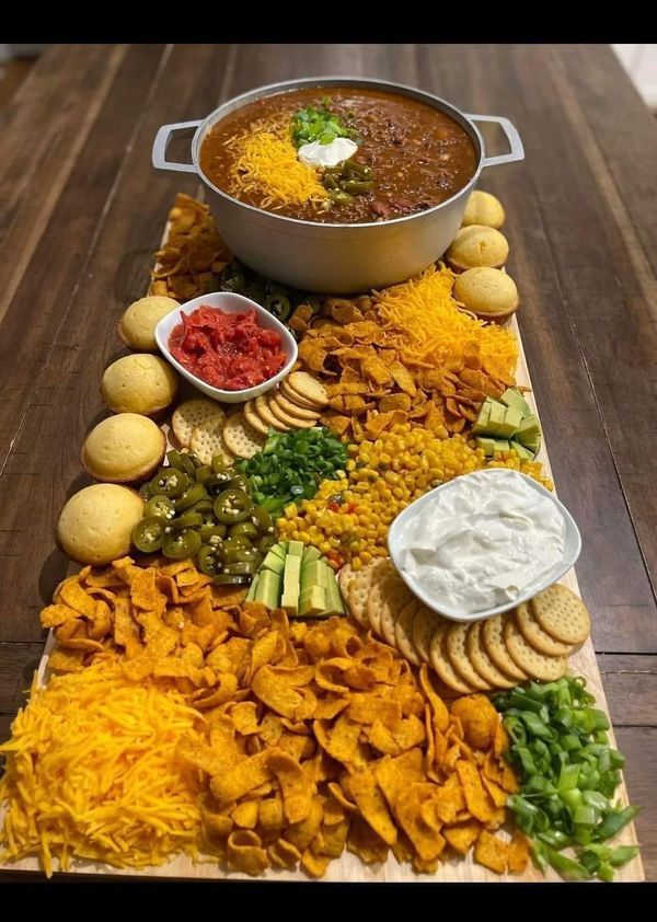 a platter filled with chips and dips on top of a wooden table next to a pot of chili