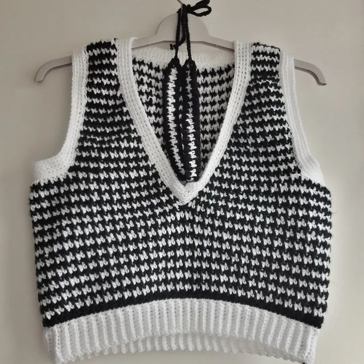 a black and white knitted sweater hanging on a hanger next to a wall