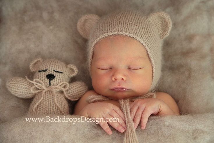 a baby sleeping next to a teddy bear wearing a knitted hat and holding it's head