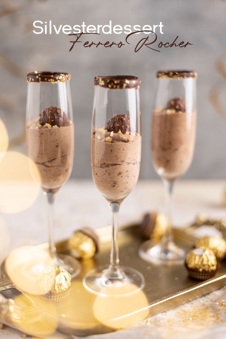 three glasses filled with dessert sitting on top of a gold tray next to chocolate candies