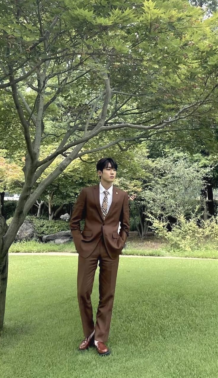 a man in a suit and tie standing next to a tree with his hands on his hips