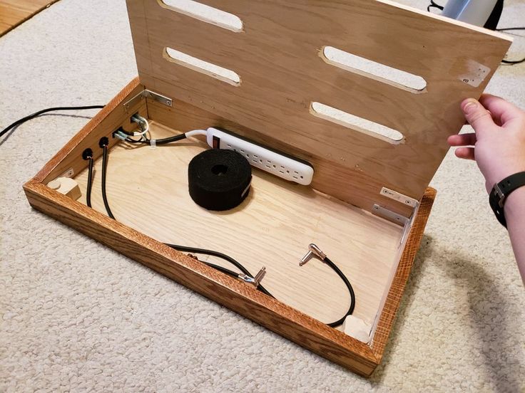 a person is holding an electronic device in a wooden box with wires and plugs