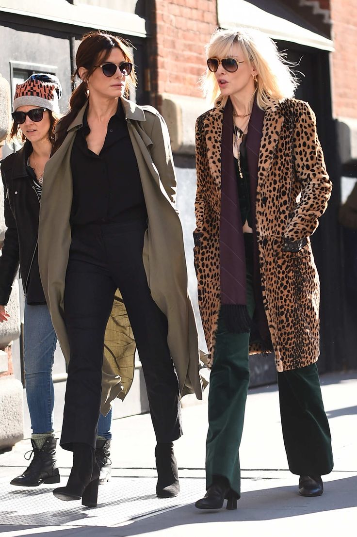 two women are walking down the street wearing leopard print coats and black pants, while one is