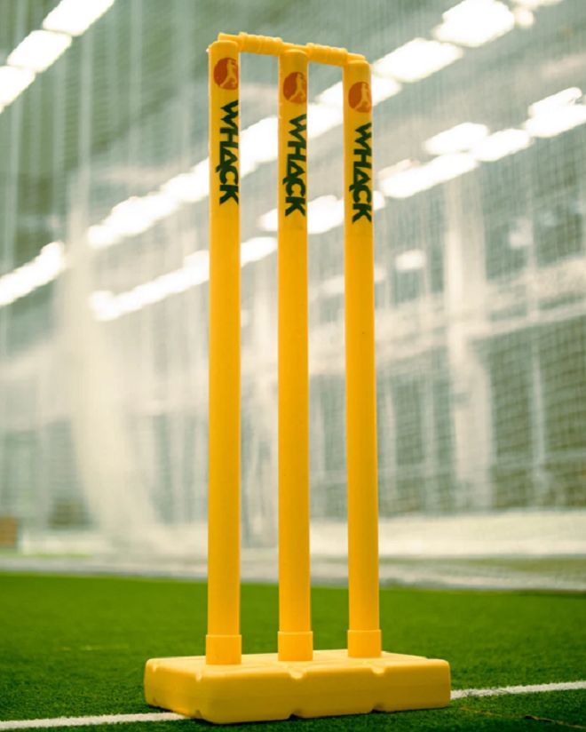 two yellow plastic cricket bats on a green grass covered field in a batting cage with white walls