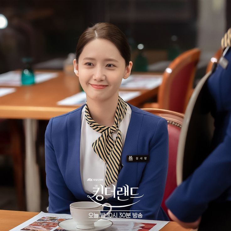 a woman sitting at a table with a cup in front of her and another person standing behind her