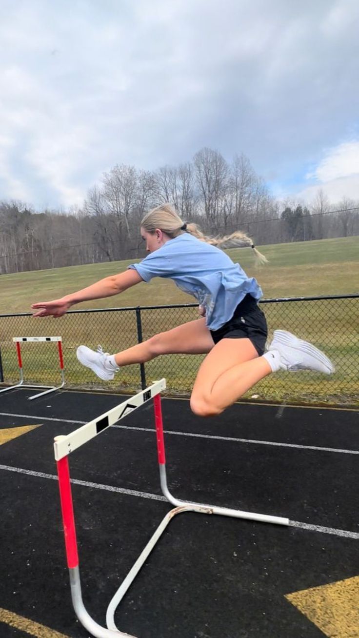 a woman jumping over an obstacle on a track