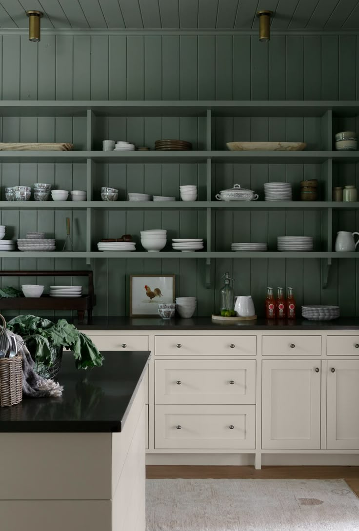 a kitchen filled with lots of white dishes and green cupboards next to a black counter top