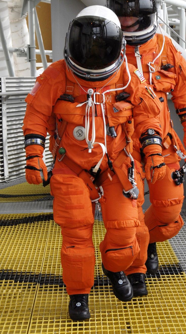 two men in orange spacesuits walking on a yellow ramp