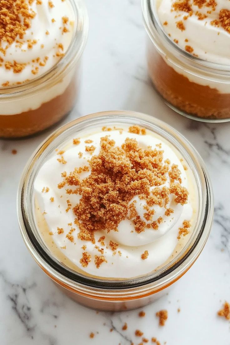 three desserts in small glass jars on a marble counter top with cinnamon sprinkles