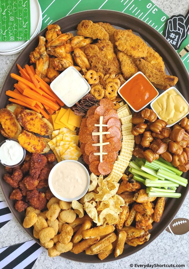 a football platter with meats, vegetables, and dips on it is ready to be eaten