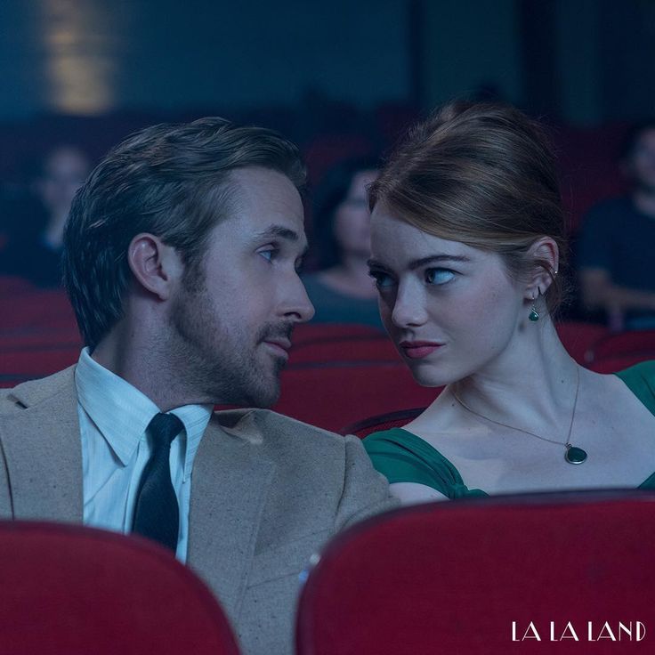 a man and woman sitting next to each other in red chairs looking at each other