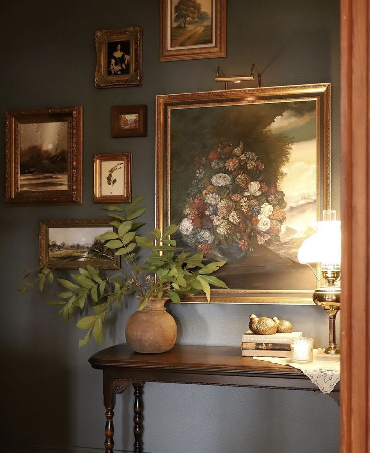 a painting hangs on the wall above a table with a lamp and vase filled with flowers