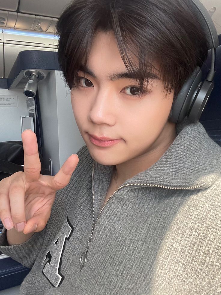 a young man wearing headphones and pointing to the side while sitting in an airplane