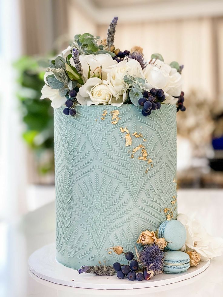 there is a blue cake with white flowers on the top and gold trimmings