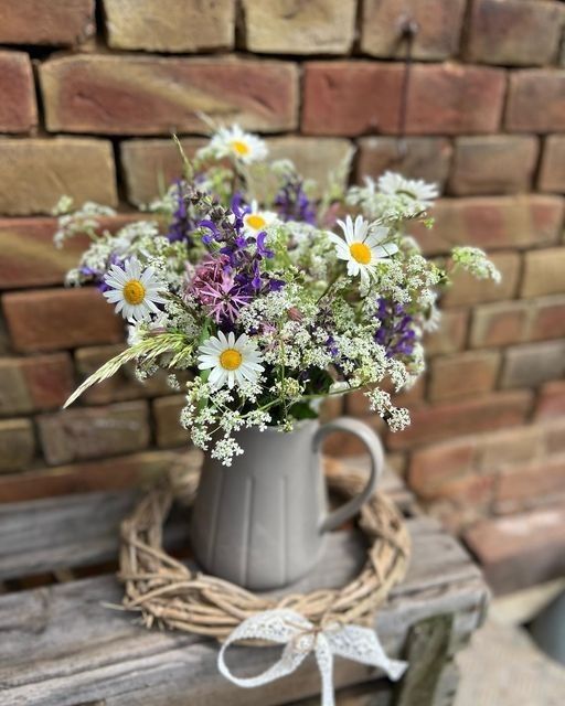 a vase filled with wildflowers sitting on top of a wooden table next to a brick wall