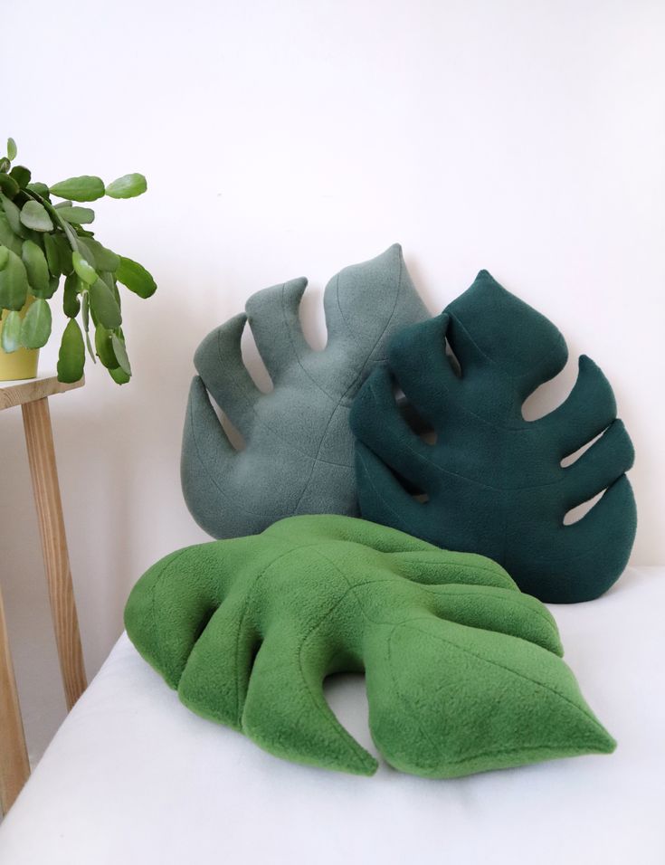 three pillows sitting on top of a white couch next to a potted green plant