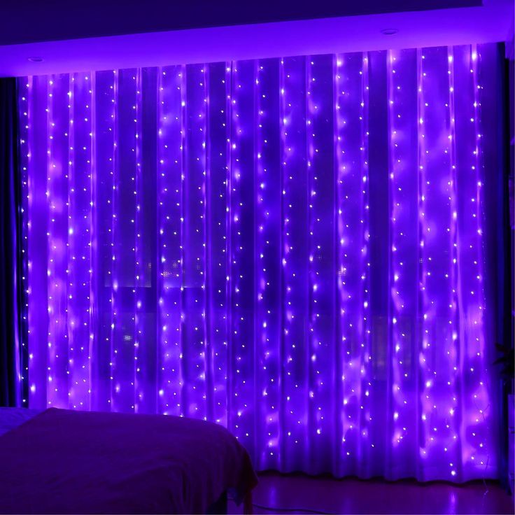 a bed sitting under a purple light next to a window covered in curtains and lights