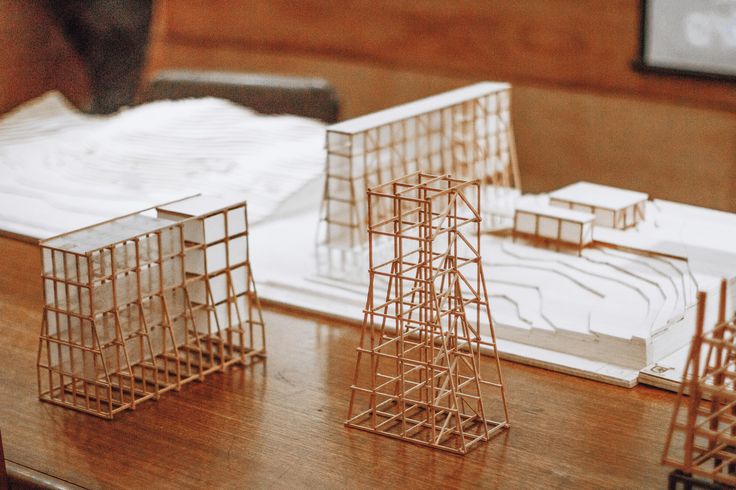 three model buildings sitting on top of a wooden table next to a notebook and pen