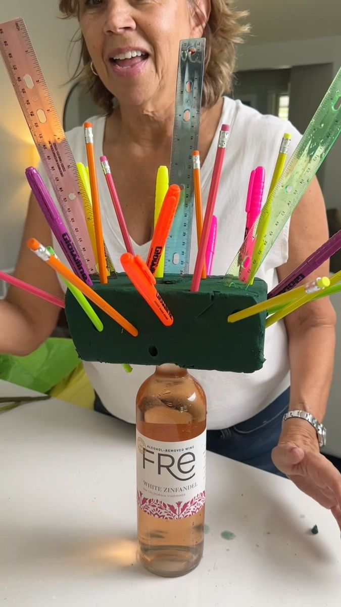 a woman sitting at a table next to a bottle with scissors and pencils sticking out of it