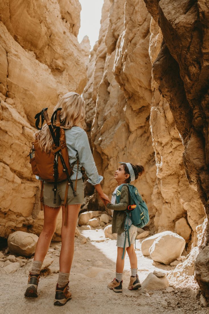 a woman and child holding hands while standing in the middle of a narrow slot between two large rocks