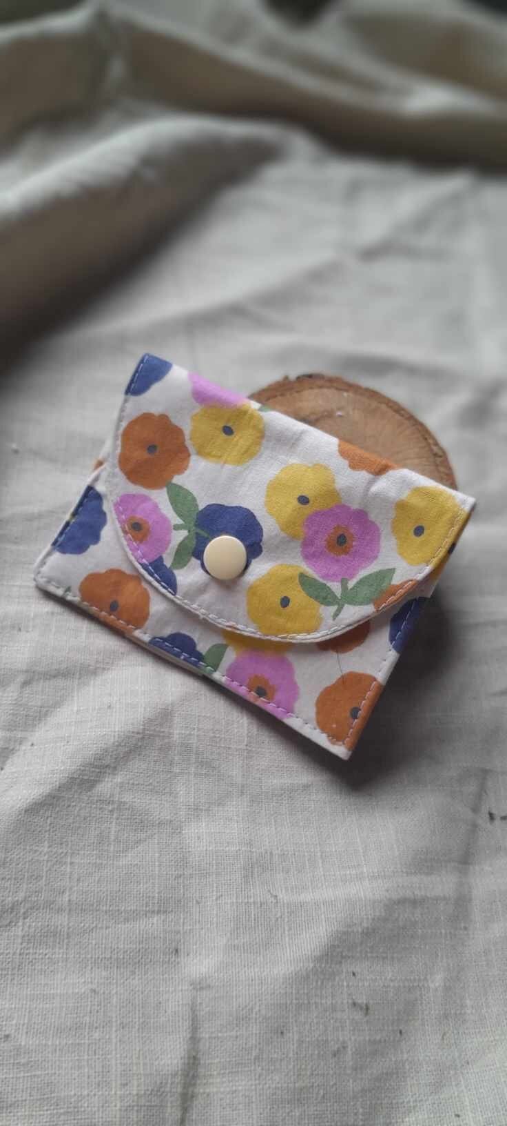 a flowered wallet sitting on top of a white cloth covered tablecloth with a wooden button in the center