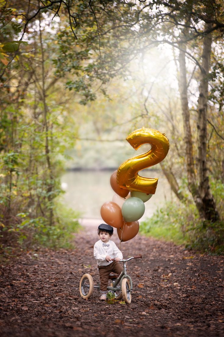 a young boy riding a bike down a dirt road with balloons attached to the back