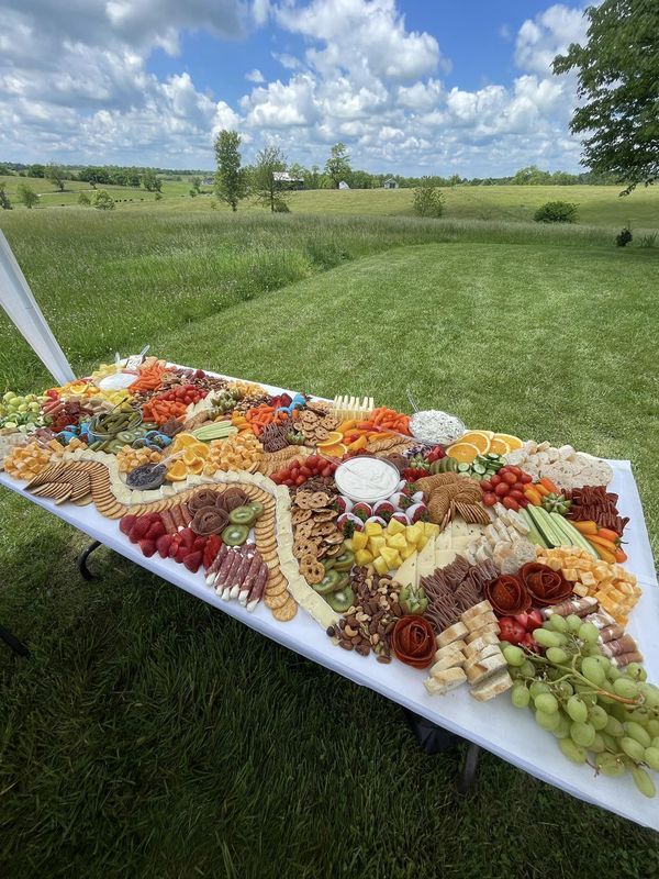 a large platter of cheese and meats on a table in the middle of a field