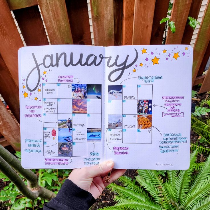 a person holding up a planner with pictures on it in front of a wooden fence