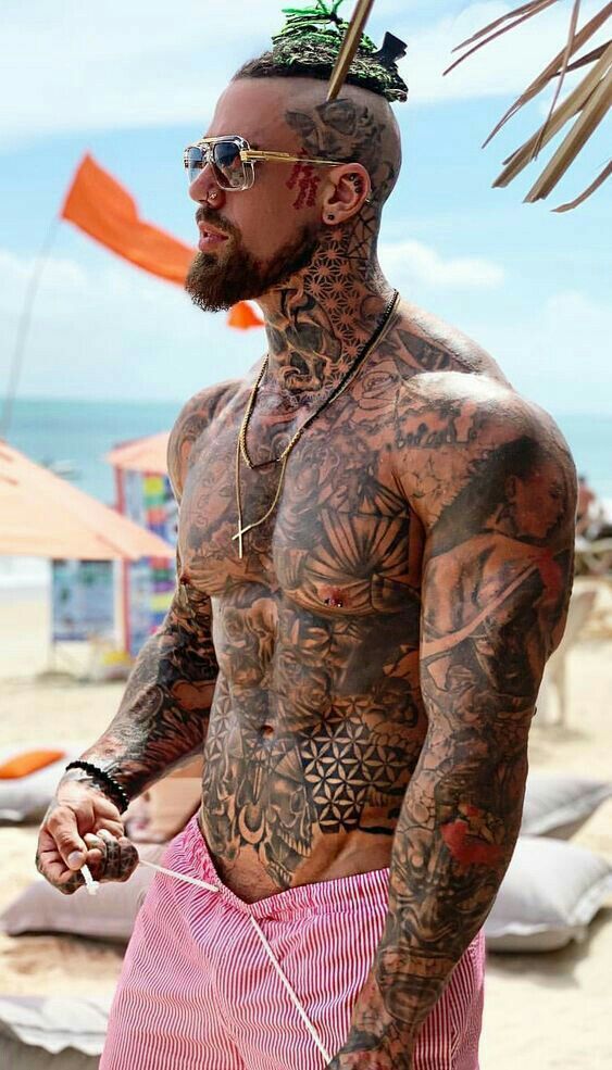 a man with tattoos on his body standing in the sand