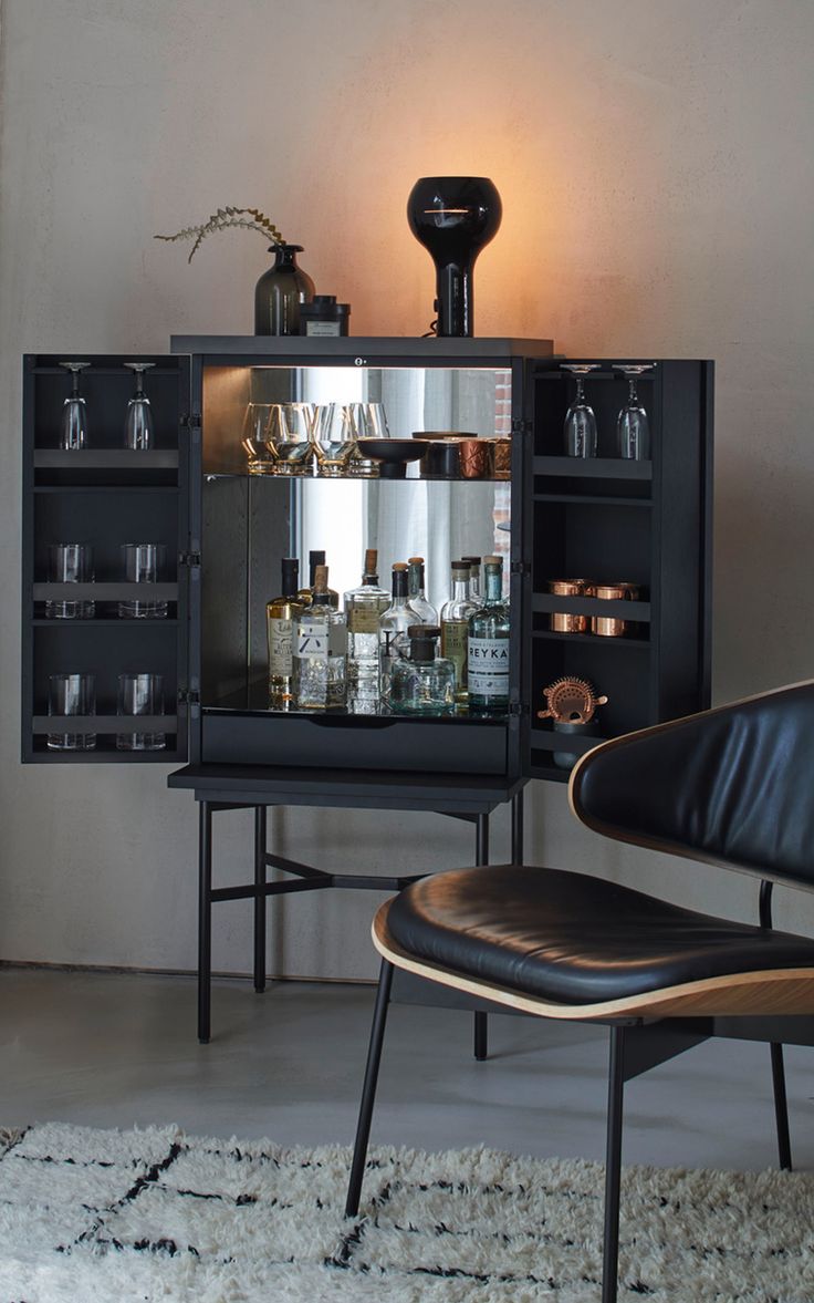 a black cabinet filled with lots of bottles and glasses next to a chair in front of it