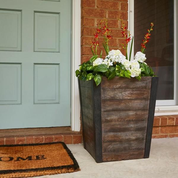 a wooden planter with flowers in it sitting on the front door step next to a welcome mat