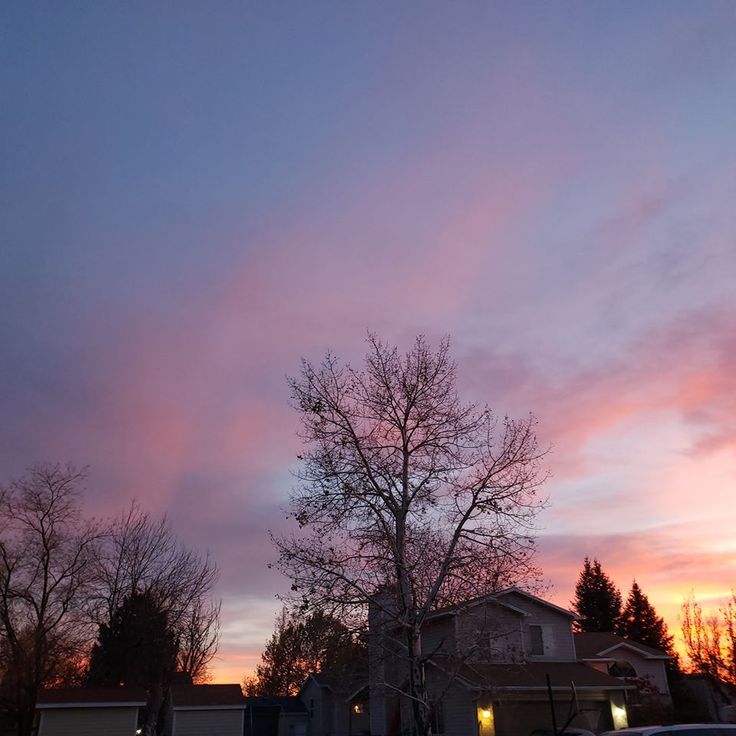 the sky is pink and purple as the sun goes down in the distance behind some trees